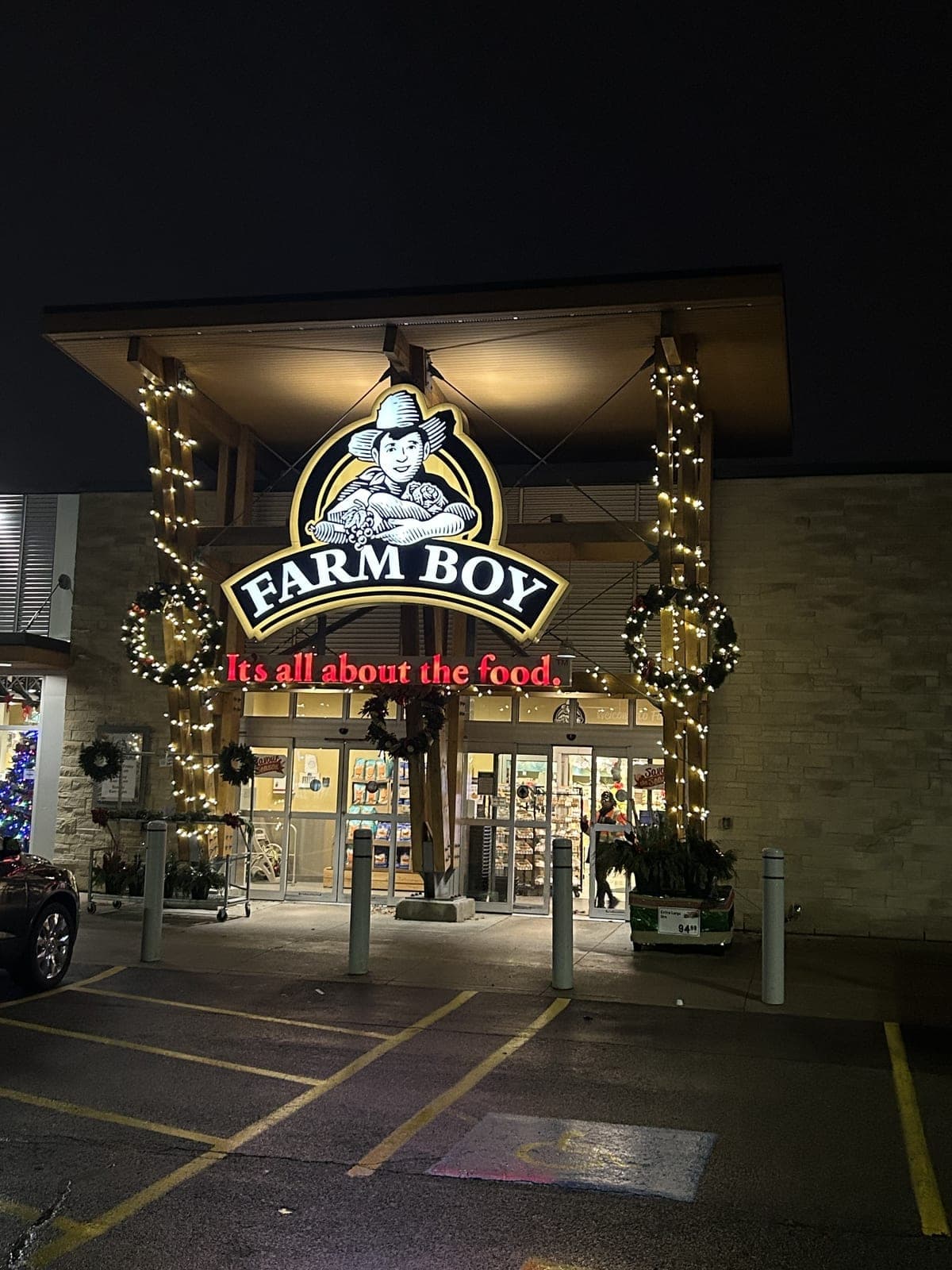 Commercial storefront entrance with columns wrapped in warm white Christmas lights and illuminated wreaths at night