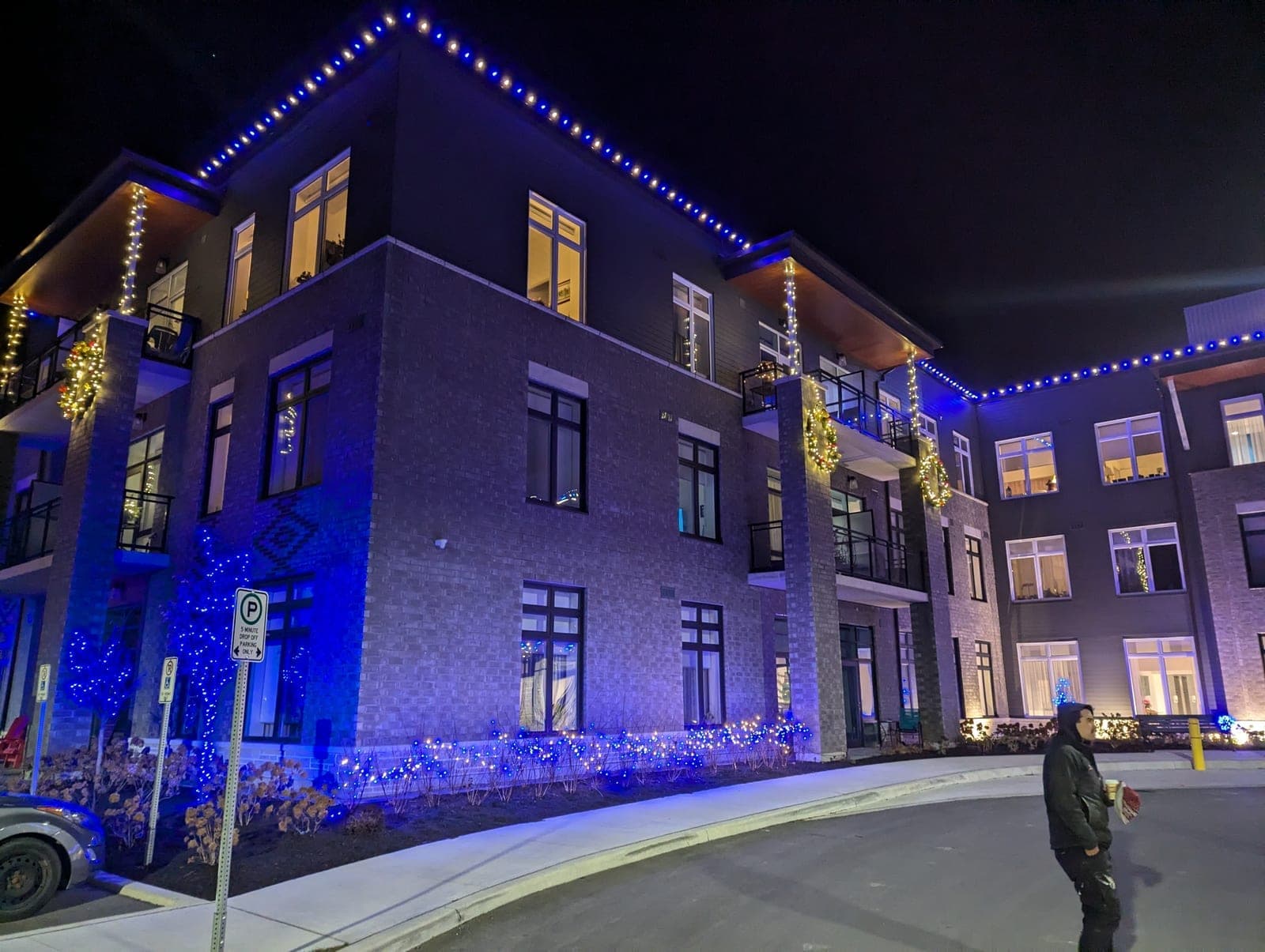 Multi-storey condo building outlined in blue and warm white Christmas lights at night.
