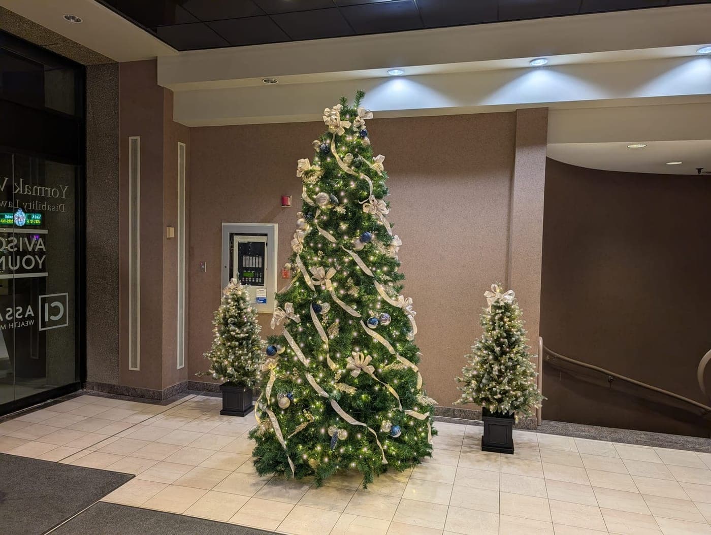 Corporate building lobby Christmas tree with gold ribbon flanked by two lit accent trees